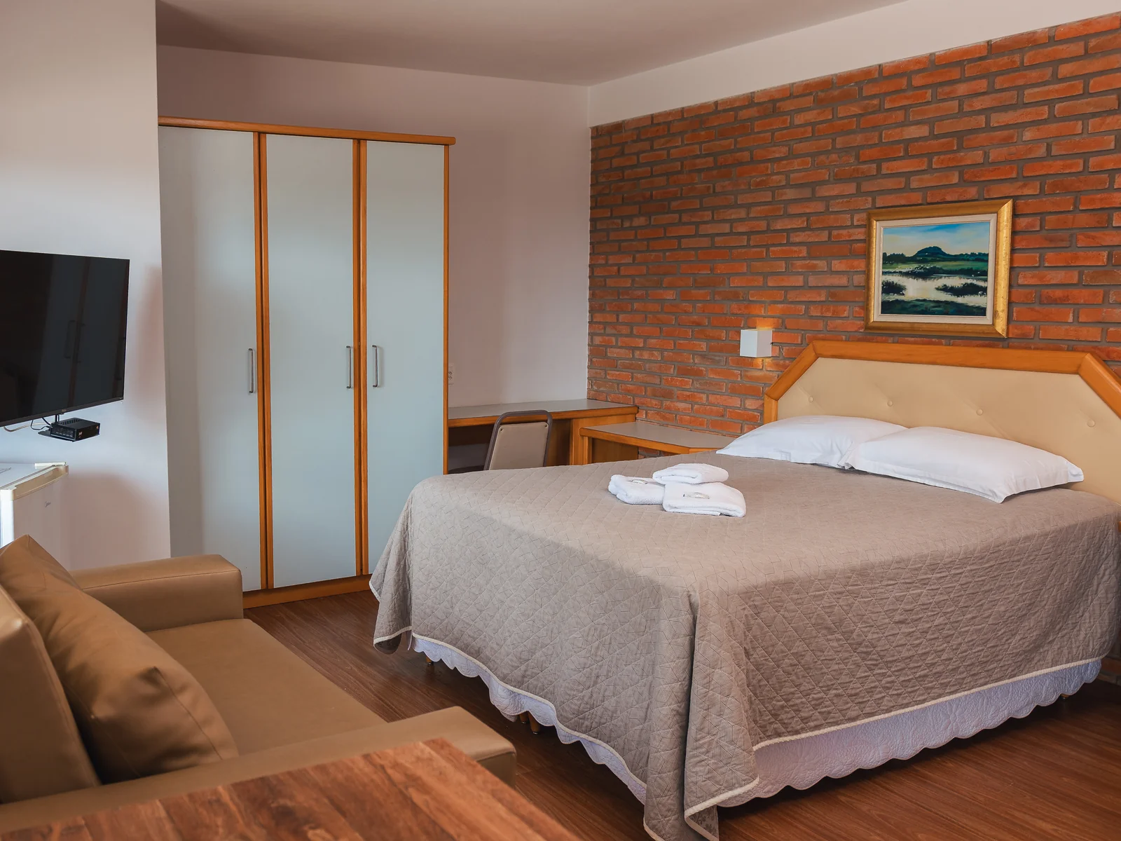 Suíte Família com cama de casal, sofá, armário e parede de tijolos no Sítio Hotel & Eventos