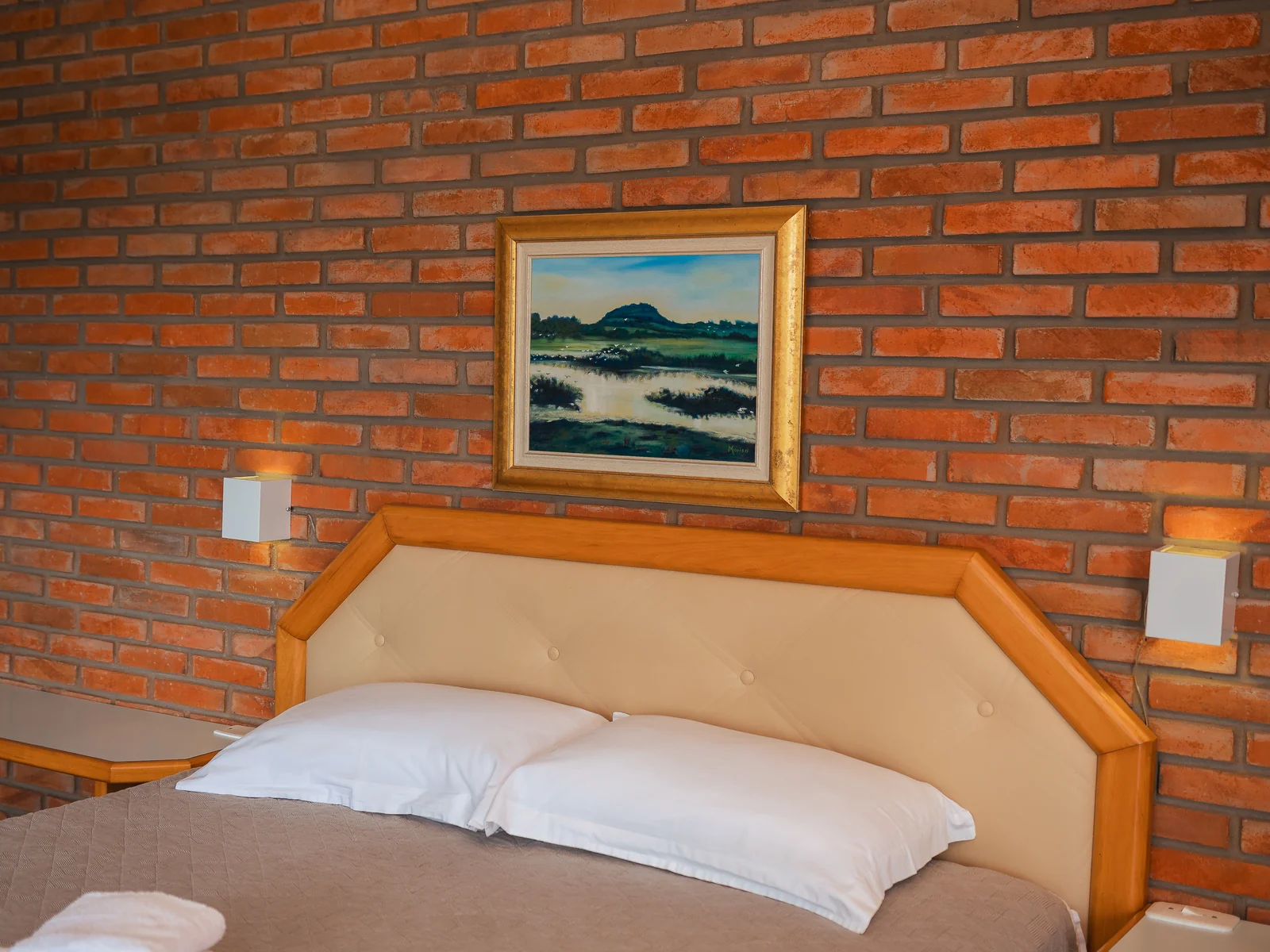 Cabeceira da cama de casal da Suíte Família com quadro e parede de tijolos aparentes